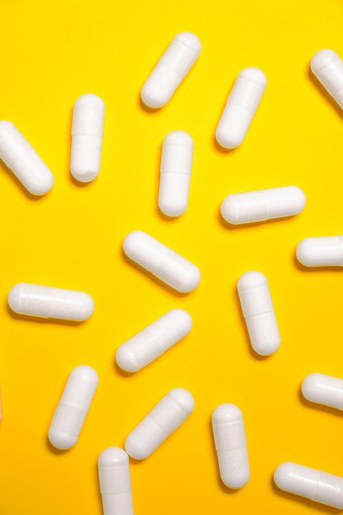 Fotografie Stock gratuită de capsule albe de medicamente pe suprafață galbenă